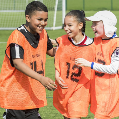 Young players in orange bibs smiling on a London playing field